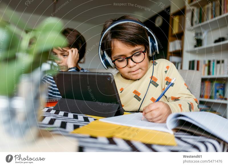 Junge schreibt Notizen mit Hilfe eines digitalen Tablets und sitzt mit einem männlichen Freund während des e-Learnings zu Hause Farbaufnahme Farbe Farbfoto