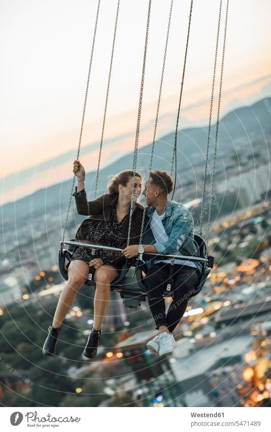 Verliebtes junges Paar reitet Kettenkarussell auf einem Rummelplatz Junges Paar Junge Paare Kettenkarussells Romanze Liebeserlebnis küssen Küsse Kuss Jahrmarkt