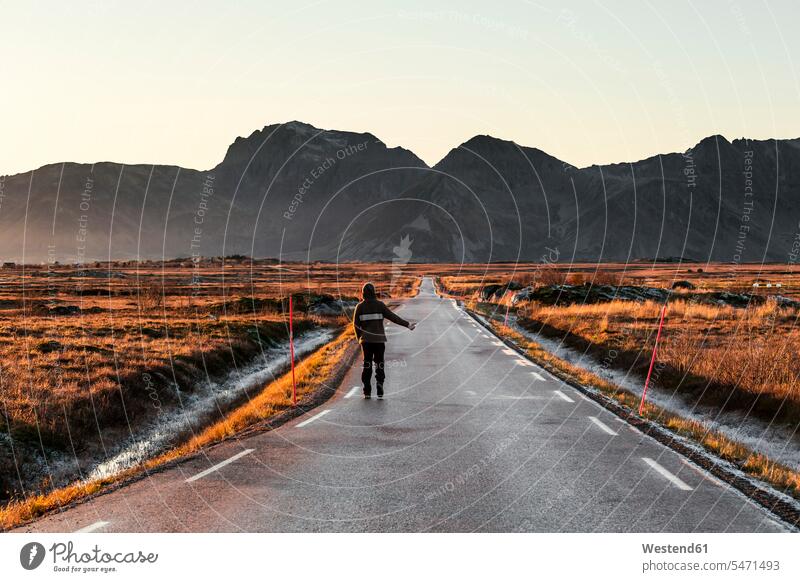 Norwegen, Lofoten-Inseln, Rückansicht eines Mannes beim Trampen auf einer leeren Landstraße Männer männlich trampen Anhalter per Autostopp fahren