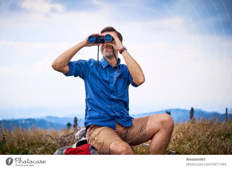 Mann schaut während Wanderung durch ein Fernglas Ferngläser Feldstecher Fernglaeser Männer männlich schauen sehend wandern Erwachsener erwachsen Mensch Menschen