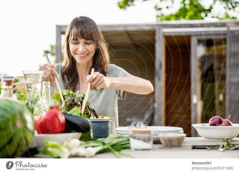 Lächelnde Frau bereitet einen Salat auf Gartentisch Leute Menschen People Person Personen Alleinstehende Alleinstehender Singles Unverheiratete Unverheirateter