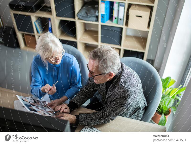 Zwei ältere Kollegen arbeiten zusammen am Schreibtisch im Büro und diskutieren über Fotos Arbeitskollegen besprechen Besprechung Arbeitstisch Schreibtische