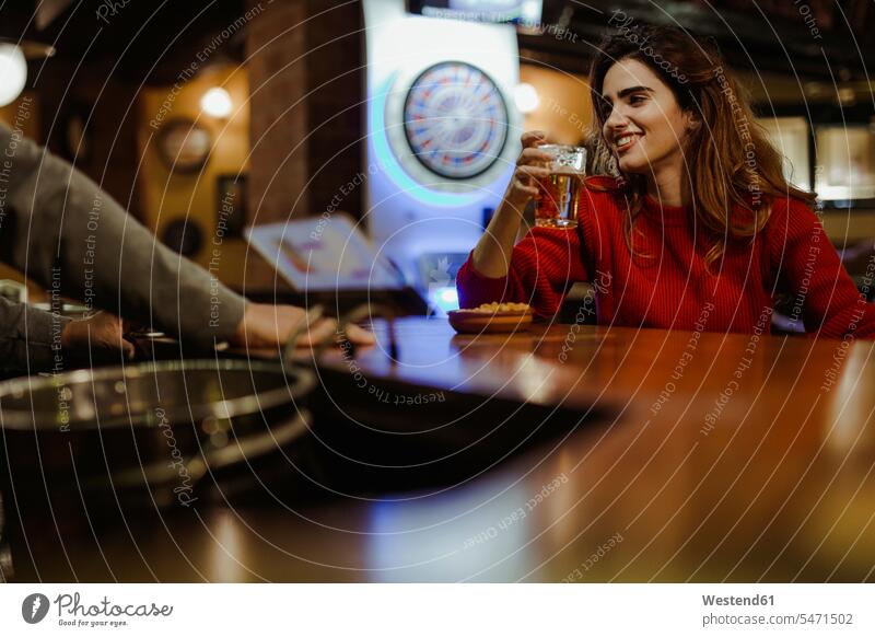 Lächelnde schöne Frau hält Bierglas in der Hand und unterhält sich mit dem Barkeeper im Restaurant Farbaufnahme Farbe Farbfoto Farbphoto Spanien