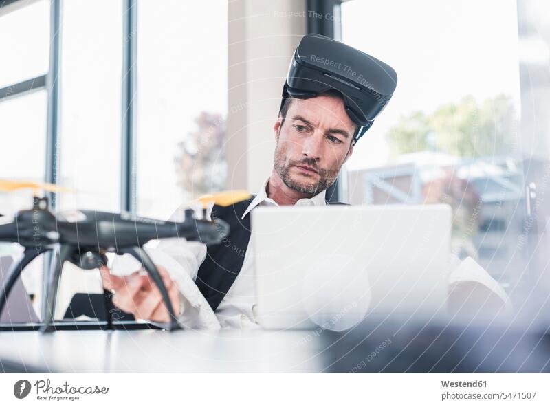 Geschäftsmann sitzt im Büro und arbeitet an einer Drohne, mit VR-Brille Drohnen Entwicklung entwickeln Entwicklungen arbeiten Arbeit Laptop benutzen
