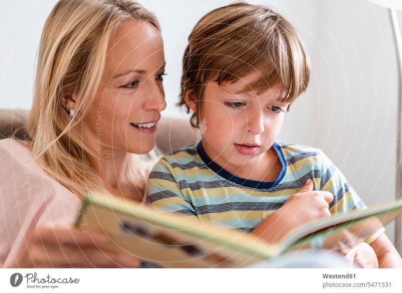 Mutter und Sohn lesen zu Hause auf der Couch gemeinsam ein Buch Bücher Couches Liege Sofas Lektüre sitzend sitzt entspannen relaxen entspanntheit relaxt freuen
