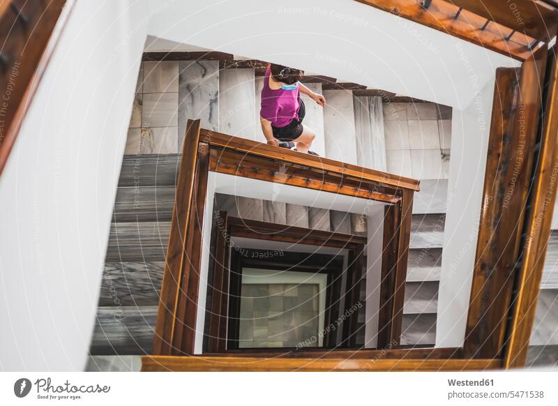 Junge Frau mit Gesichtsmaske geht von der Wendeltreppe des Gebäudes herunter Farbaufnahme Farbe Farbfoto Farbphoto Innenaufnahme Innenaufnahmen innen drinnen