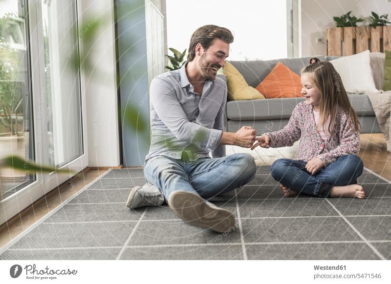 Junger Mann und kleines Mädchen sitzen zu Hause, spielen Papier Schere Stein optimistisch Optimismus Schere Stein Papier Ganzkörperansicht Ganzansicht