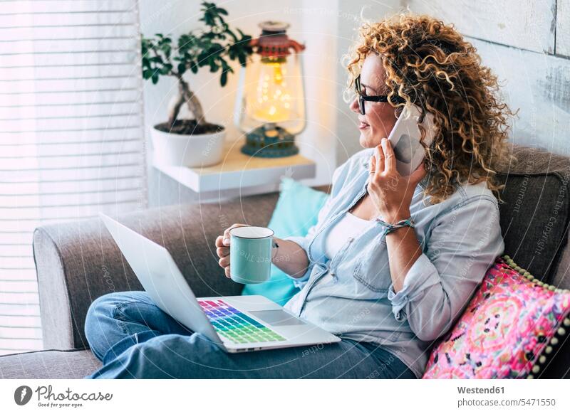 Frau auf der Couch zu Hause mit Kaffeebecher, Laptop und Mobiltelefon Gefärbtes Haar Gefärbte Haare Vorhang Gardinen Vorhänge Gemütlich Wohlfühlen behaglich
