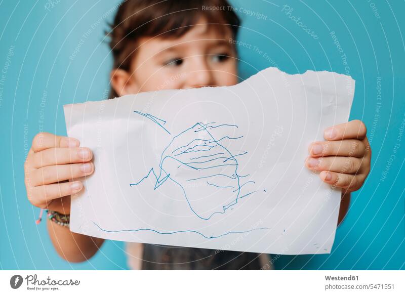 Kleines Mädchen hält eine handgemachte Zeichnung auf blauem Hintergrund Bilder Bildnis Zeichnungen Kinderzeichnungen Papiere gefühlvoll Emotionen Empfindung