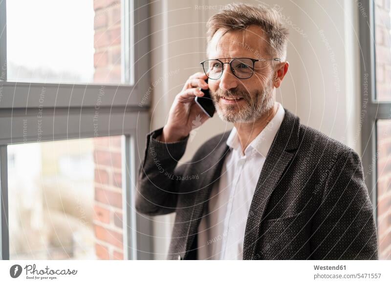 Geschäftsmann am Mobiltelefon am Fenster im Büro Office Büros Businessmann Businessmänner Geschäftsmänner Handy Handies Handys Mobiltelefone telefonieren
