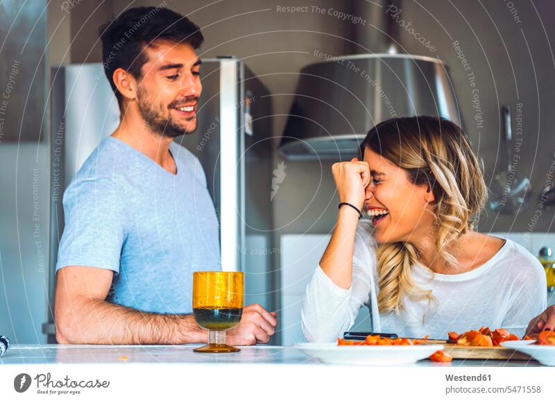 Lachende junge Frau mit Freund in der Küche zu Hause Gläser Trinkglas Trinkgläser reden freuen Frohsinn Fröhlichkeit Heiterkeit geniessen Genuss Glück