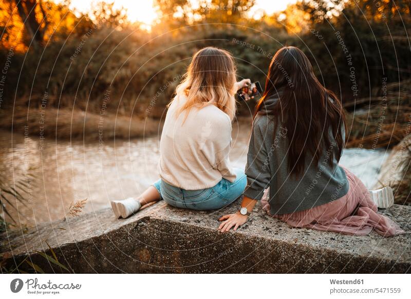 Schwestern, die bei Sonnenuntergang auf einer Stützmauer im Wald sitzen Farbaufnahme Farbe Farbfoto Farbphoto Außenaufnahme außen draußen im Freien
