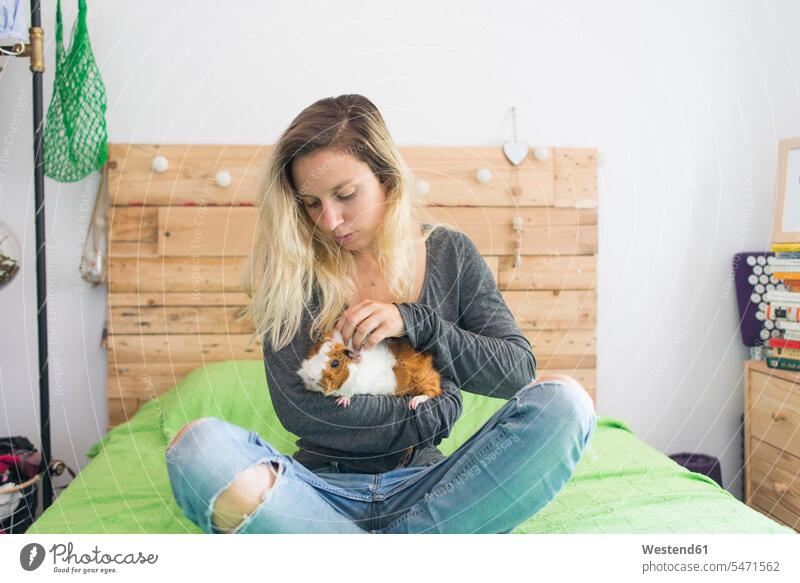 Frau hält Meerschweinchen im Arm, während sie zu Hause auf dem Bett sitzt Farbaufnahme Farbe Farbfoto Farbphoto Innenaufnahme Innenaufnahmen innen drinnen Tag