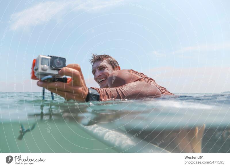Surfer mit auf dem Surfbrett liegender Action-Kamera Surfing Wellenreiten surfboard surfboards Surfbretter Fotokamera Kameras freuen Glück glücklich sein
