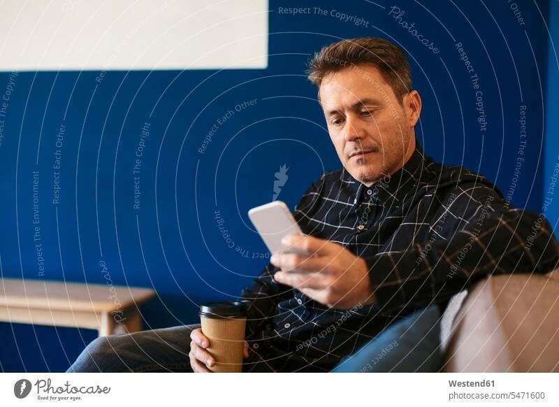 Geschäftsmann mit Kaffee zum Mitnehmen sitzt und auf sein Handy schaut sitzen sitzend Businessmann Businessmänner Geschäftsmänner Mobiltelefon Handies Handys