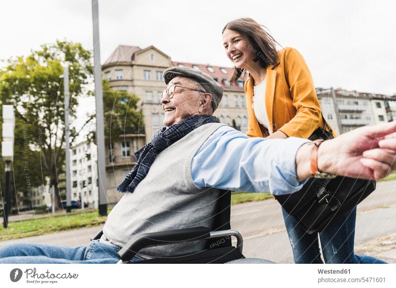 Lachende junge Frau schiebt glücklichen älteren Mann im Rollstuhl Leute Menschen People Person Personen Europäisch Kaukasier kaukasisch 2 2 Menschen 2 Personen