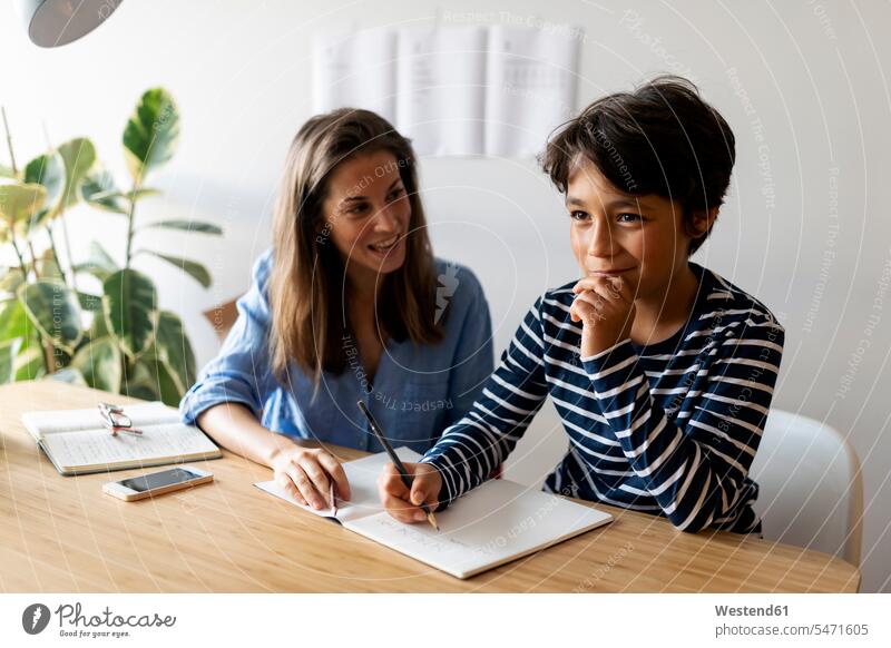 Weibliche Tutorin hilft dem Jungen zu Hause beim Schreiben von Hausaufgaben Farbaufnahme Farbe Farbfoto Farbphoto Spanien Freizeitkleidung Freizeitbekleidung