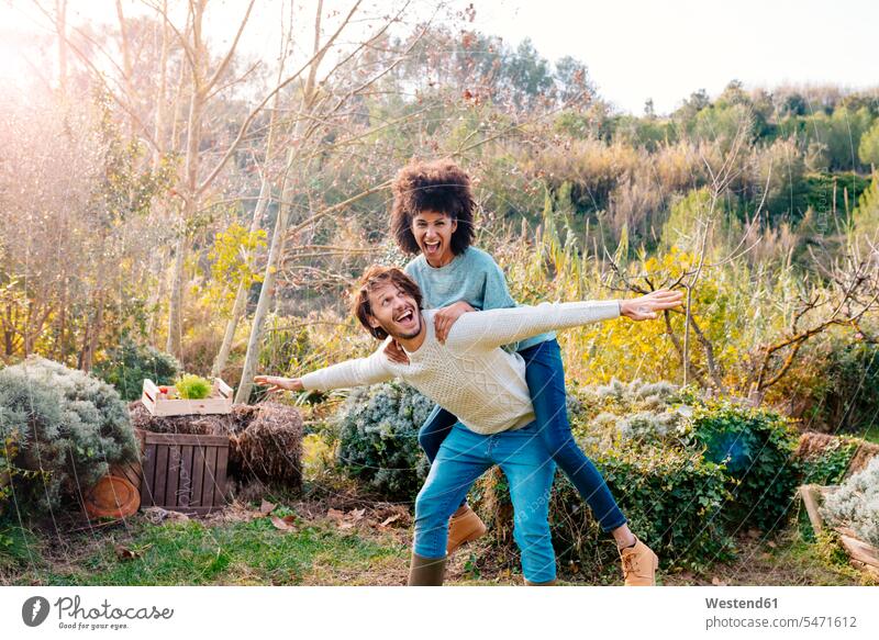 Mann trägt Freundin Huckepack in einem Garten auf dem Lande spielen Unbeschwert Sorglos albern herumalbern Albernheit tragen transportieren Gärten Gaerten Paar