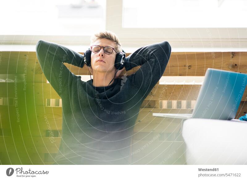 Entspannter junger Mann, der auf dem Boden sitzt und mit Kopfhörern Musik hört Männer männlich entspannt entspanntheit relaxt sitzen sitzend Laptop Notebook