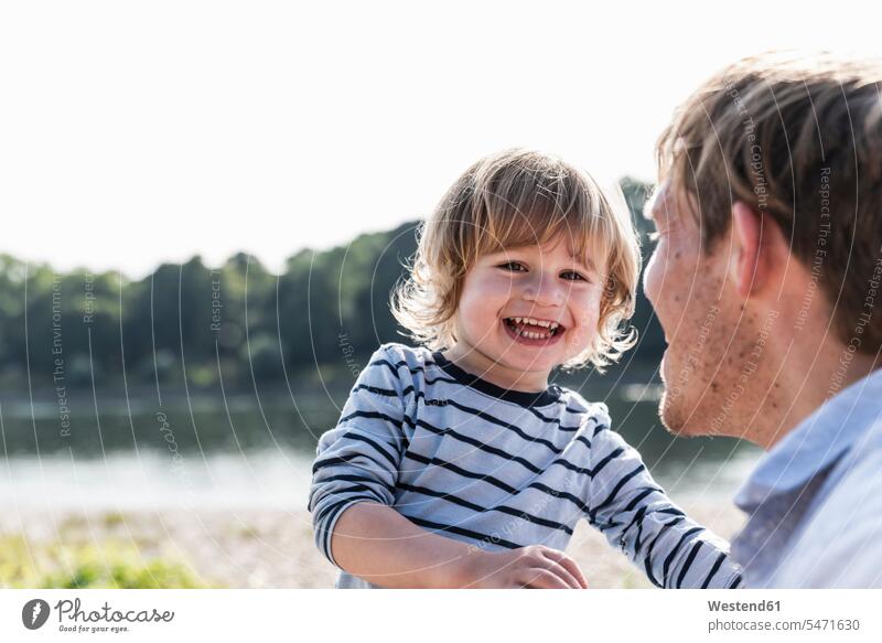 Vater und Sohn haben Spaß am Flussufer Spass Späße spassig Spässe spaßig Papas Väter Vati Vatis Papis Sommer Sommerzeit sommerlich Söhne lachen spielen Eltern