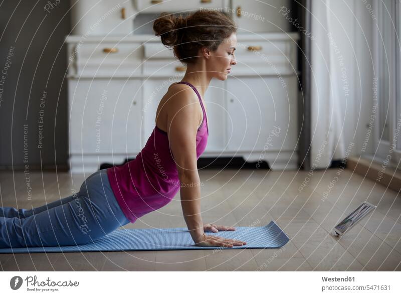 Mittlere erwachsene Frau, die sich zu Hause beim Yoga ein digitales Tablet anschaut Farbaufnahme Farbe Farbfoto Farbphoto Innenaufnahme Innenaufnahmen innen