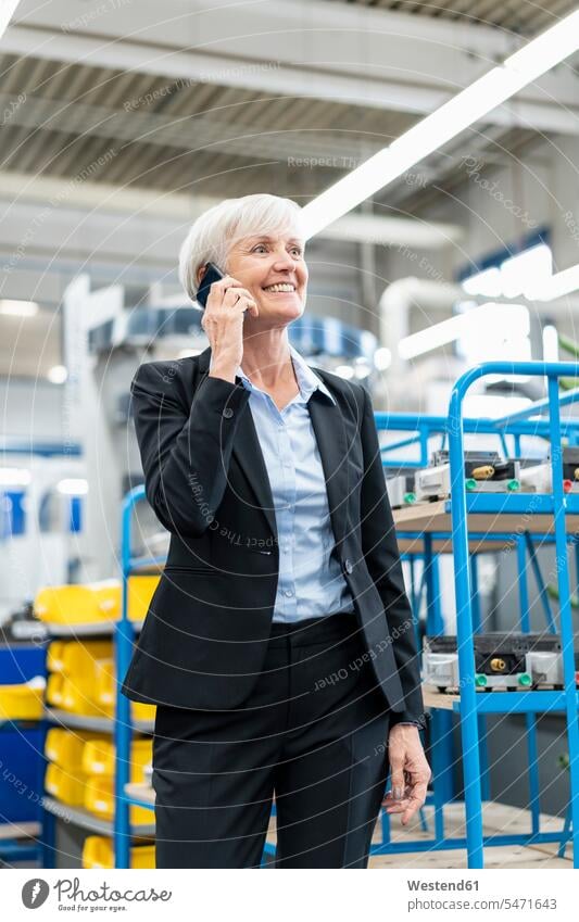 Lächelnde ältere Geschäftsfrau am Handy in einer Fabrik Fabriken telefonieren anrufen Anruf telephonieren Geschäftsfrauen Businesswomen Businessfrauen
