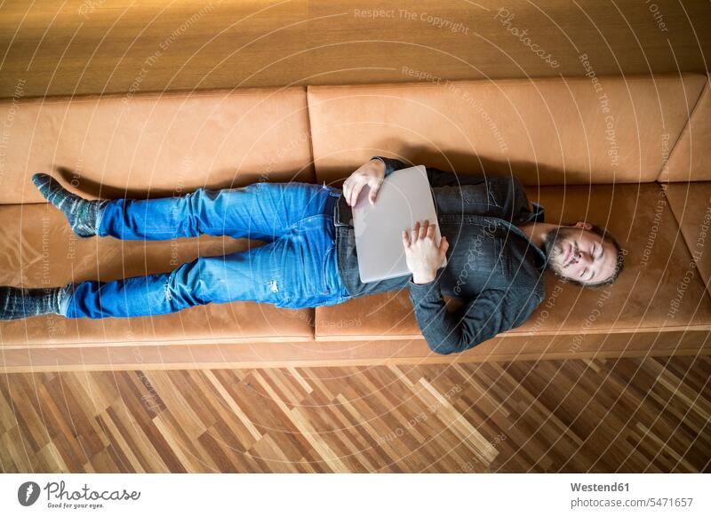 Mann mit Laptop entspannt sich auf der Couch Männer männlich liegen liegend liegt Entspannung relaxen entspannen Notebook Laptops Notebooks Sofa Couches Liege