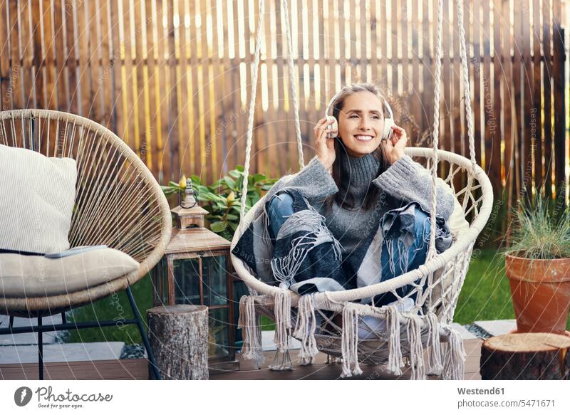 Lächelnde schöne Frau hört Musik, während sie auf einer Schaukel im Garten sitzt Europäer Europäisch Kaukasier kaukasisch eine Person ein Mensch nur eine Person