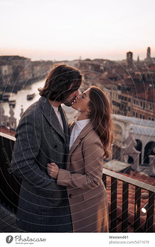 Zärtliches junges Paar küsst sich auf einem Balkon über der Stadt Venedig, Italien Jacken Kuss Küsse abends geniessen Genuss Glück glücklich sein glücklichsein