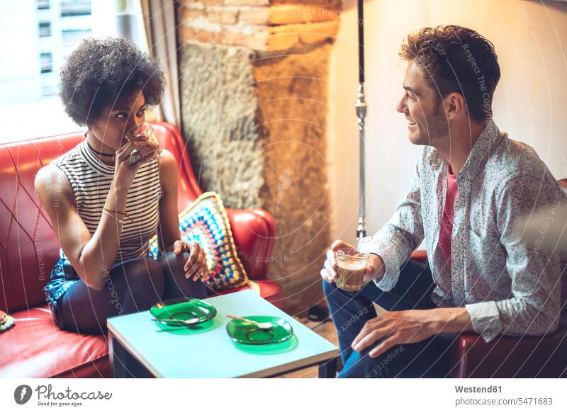 Lächelnder Mann sieht Freundin beim Kaffeetrinken an, während er im Café sitzt Farbaufnahme Farbe Farbfoto Farbphoto Innenaufnahme Innenaufnahmen innen drinnen