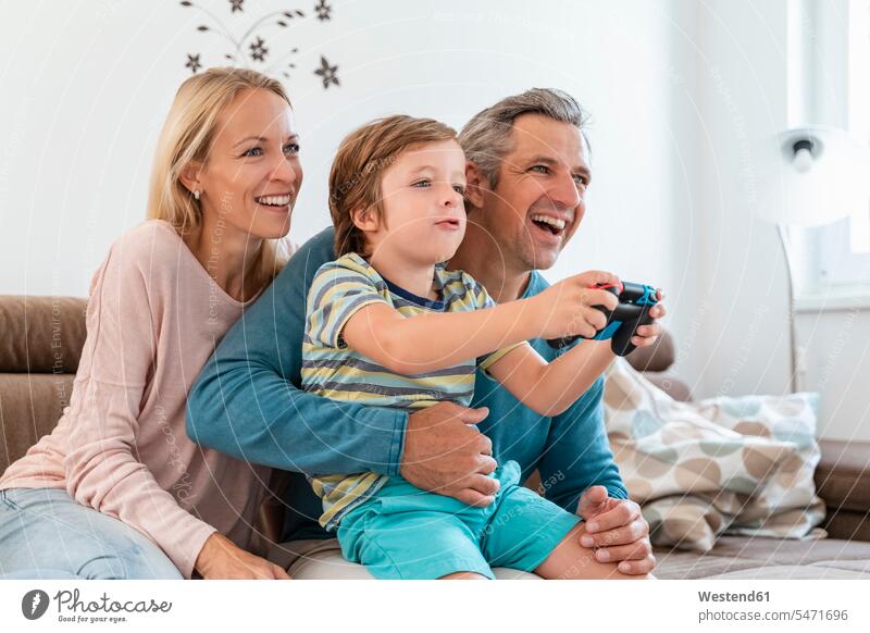 Glückliche Eltern mit Sohn spielen zu Hause auf der Couch Videospiele Couches Liege Sofas sitzend sitzt entspannen relaxen entspanntheit relaxt freuen Frohsinn