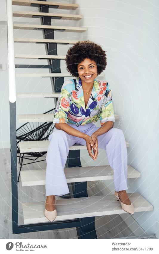 Glückliche Frau mittleren Alters sitzt auf schwebender Treppe in modernem Penthouse Farbaufnahme Farbe Farbfoto Farbphoto Innenaufnahme Innenaufnahmen innen