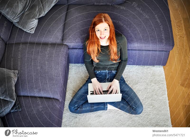 Rothaarige Frau sitzt mit Laptop auf dem Boden im Wohnzimmer weiblich Frauen Notebook Laptops Notebooks sitzen sitzend rothaarig rote Haare rothaarige