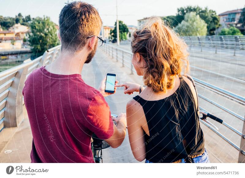 Ehepaar benutzt Smartphone, während es bei Sonnenuntergang mit Fahrrädern auf der Brücke steht Farbaufnahme Farbe Farbfoto Farbphoto Freizeitbeschäftigung Muße