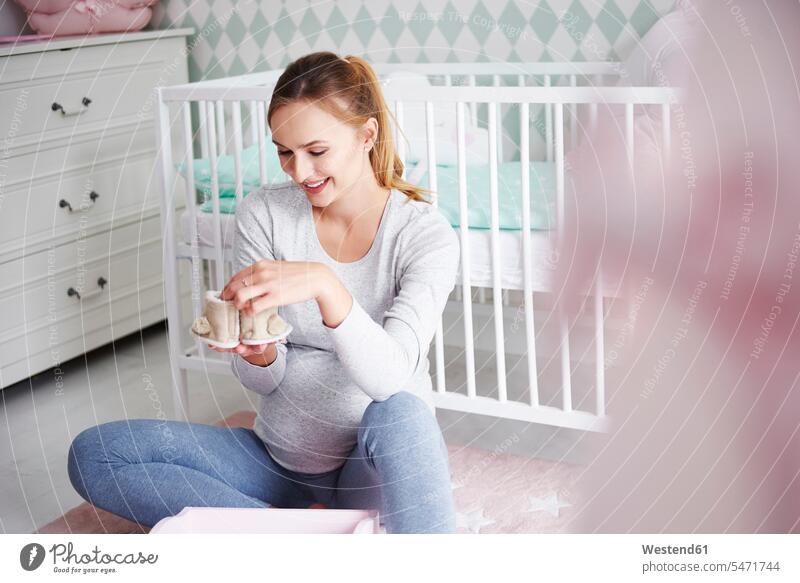 Schwangere Frau mit Babyschuhen im Babyzimmer Erwartung erwartungsvoll erwarten Vorfreude betrachten betrachtend weiblich Frauen lächeln schwanger