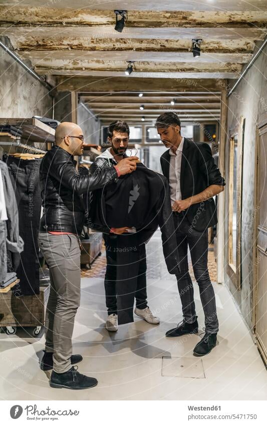 Designer und Stylistin in modernem Herrenbekleidungsgeschäft mit neuer Kollektion für Männer Kunde Kunden Kundschaft zeigen vorführen präsentieren Vorführung