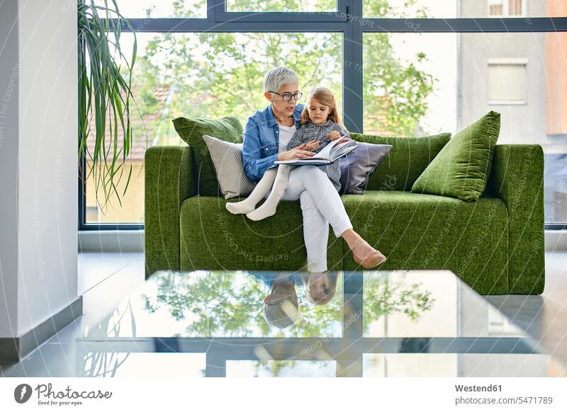 Großmutter sitzt mit Enkelin auf der Couch und liest gemeinsam ein Buch Generation Bücher Couches Liege Sofas Lektüre sitzend behüten behütet geborgen