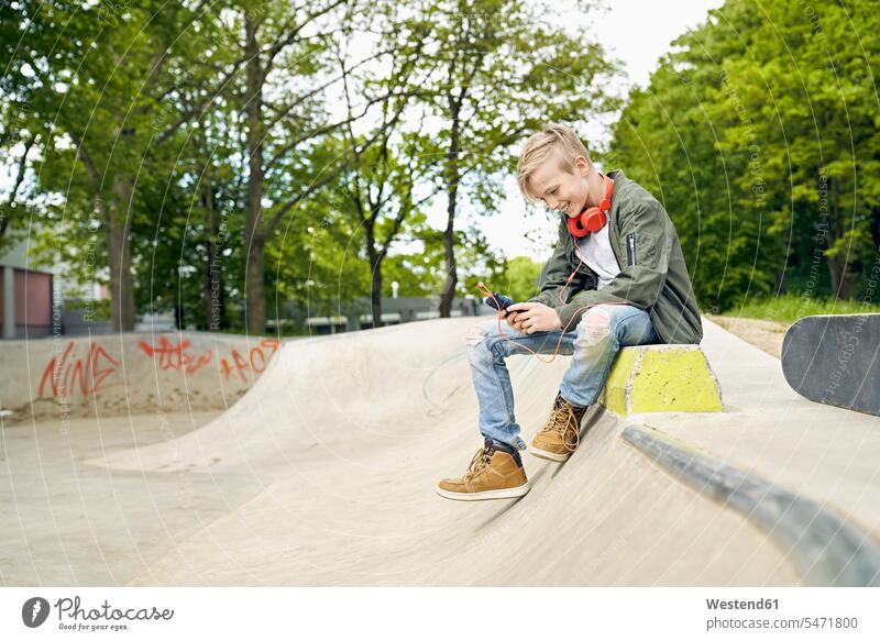 Junge mit Kopfhörern im Skatepark mit Smartphone Skateboarder Skateboardfahrer Skateboarders Skater iPhone Smartphones lächeln cool Coolness Kopfhoerer Buben