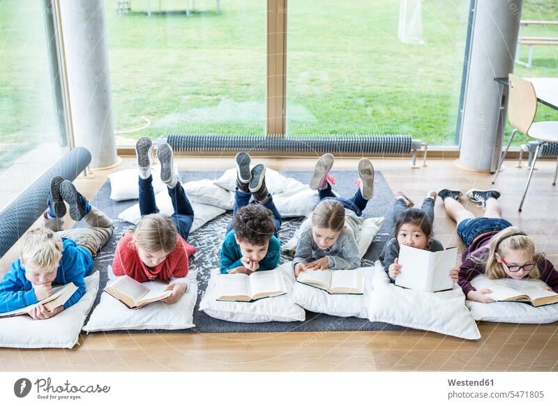Auf dem Boden liegende Schülerinnen und Schüler lesen Bücher im Pausenraum der Schule Buch Schulkind Bildung Freizeit nebeneinander Gemeinsam Fenster brav