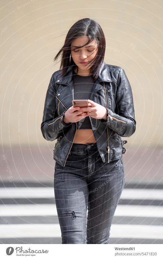 Junge Frau, die den Fußgängerüberweg überquert und ein Mobiltelefon benutzt Fussgaengerueberweg benutzen benützen Smartphone iPhone Smartphones weiblich Frauen