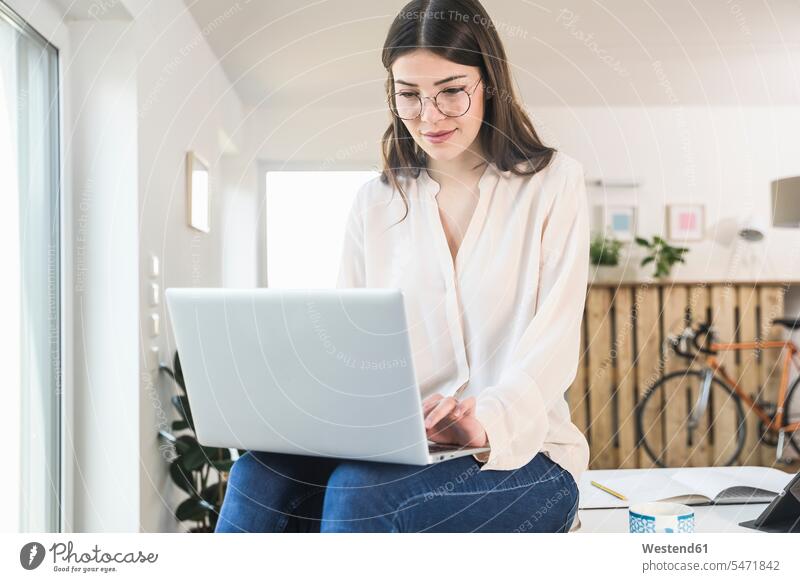 Junge Frau sitzt auf dem Tisch zu Hause mit Laptop sitzen sitzend Tische Notebook Laptops Notebooks weiblich Frauen Zuhause daheim Computer Rechner Erwachsener