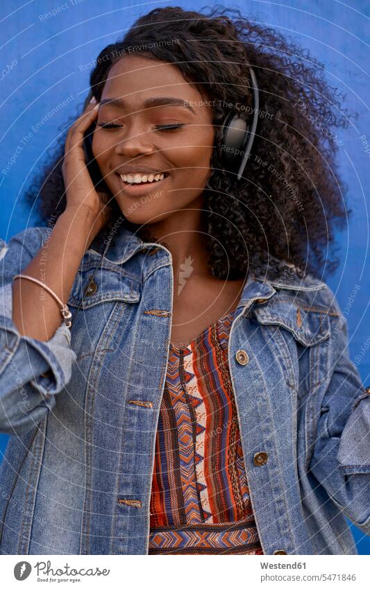 Porträt einer lächelnden jungen Frau, die mit Kopfhörern Musik hört Leute Menschen People Person Personen Afrikanisch Afrikanische Abstammung dunkelhäutig