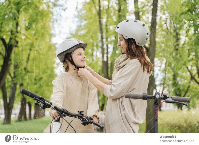 Mutter trägt Helm für ihre Tochter gegen Bäume im Stadtpark Farbaufnahme Farbe Farbfoto Farbphoto Freizeitbeschäftigung Muße Zeit Zeit haben Freizeitkleidung