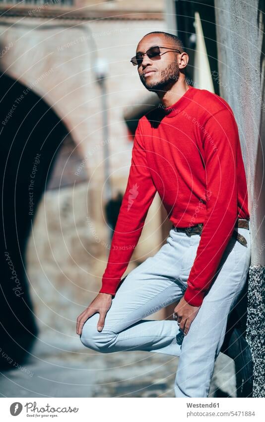 Porträt eines modischen jungen Mannes mit rotem Pullover und Socken, der das Sonnenlicht genießt genießen geniessen Genuss roter rotes Portrait Porträts