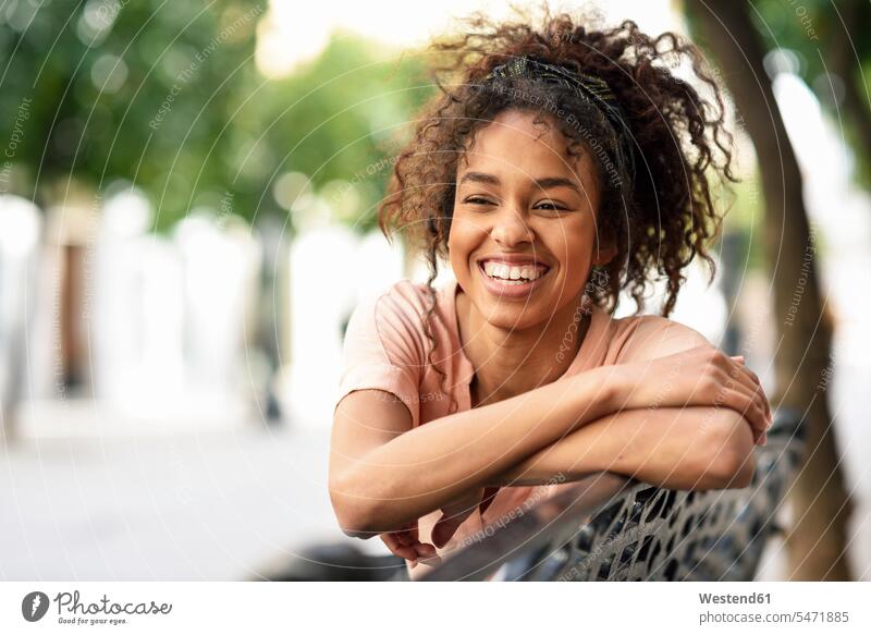 Porträt einer glücklichen jungen Frau, die auf einer Bank sitzt Glück glücklich sein glücklichsein Sitzbänke Bänke Sitzbank sitzen sitzend weiblich Frauen