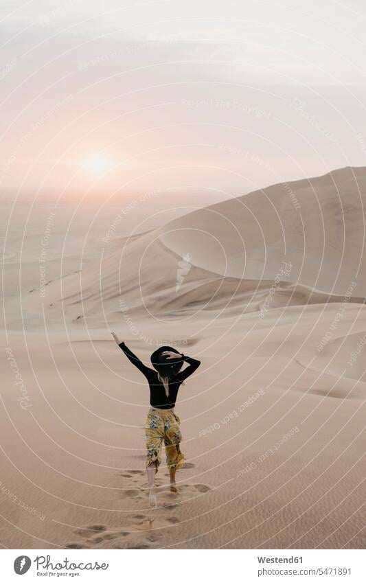 Namibia, Namib, Rückenansicht einer modischen Frau, die auf eine Wüstendüne springt Wüstendünen Wuestenduene Wuestenduenen Düne Duenen Dünen weiblich Frauen