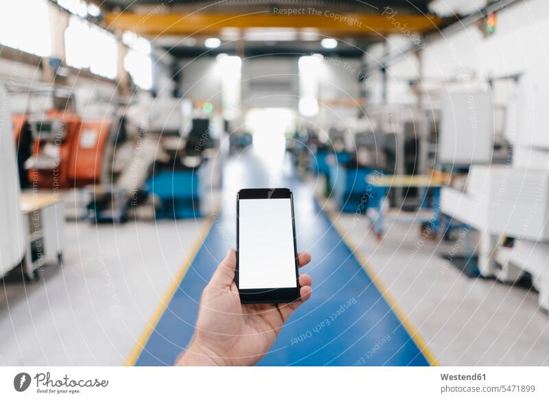 Hand hält Smartphone mit leerem Bildschirm in einer Fabrikhalle Europäer Kaukasier Europäisch kaukasisch Handy Mobiltelefon Handies Handys Mobiltelefone