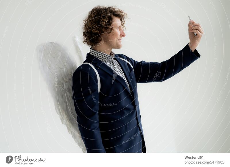 Geschäftsmann mit Engelsflügeln, der ein Selfie macht Selbstportrait Selfies sich selbst fotografieren Flügel Fluegel Engelsfluegel Anzug Anzuege Anzüge stehen