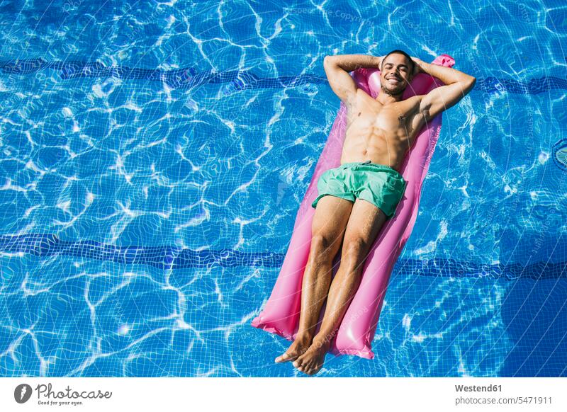Attraktiver junger Mann ohne Hemd mit Händen hinter dem Kopf, der sich auf einem Luftbett im Schwimmbad entspannt Farbaufnahme Farbe Farbfoto Farbphoto Spanien