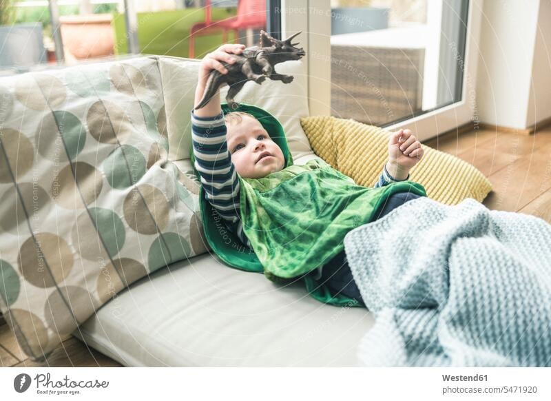 Junge in einem Kostüm liegend auf einer Matratze spielen mit Spielzeug-Figur zu Hause liegt Tierfigur Tierfiguren Maskenkostüm Maskenkostüme Verkleidung Kostüme